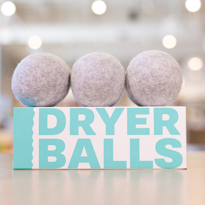 Three dark grey dryer balls lined up on top of box