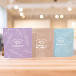 Three Epsom Salt pouches with purple, brown, and blue colors in a row on wooden counter