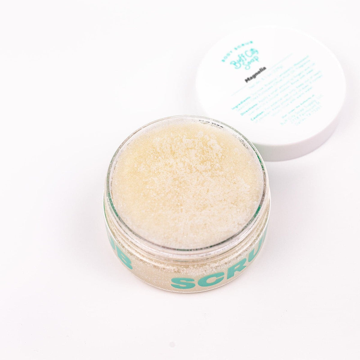 can of Buff City Soap's magnolia body scrub with a purple bar of soap resting on it