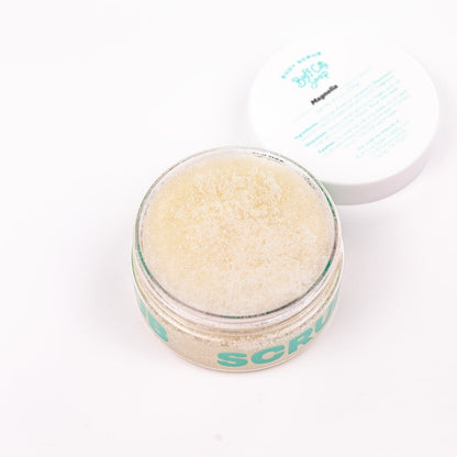 can of Buff City Soap's magnolia body scrub with a purple bar of soap resting on it